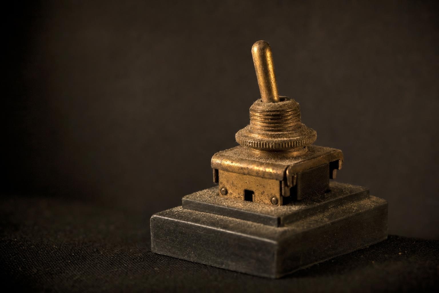 A single dust-covered brass toggle switch under warm light against a dark background