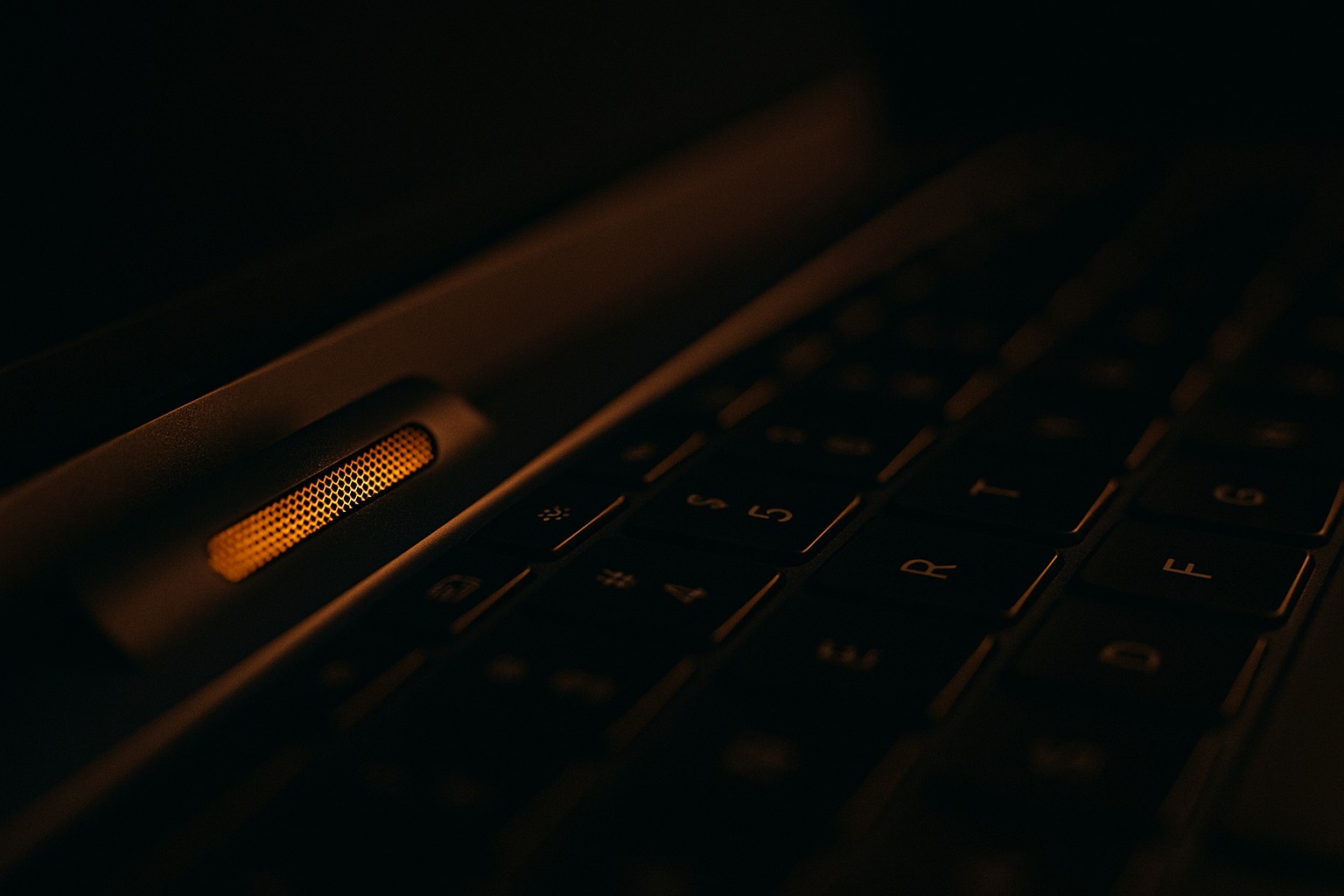 A laptop microphone grille glowing faintly, the keyboard blurred behind it.