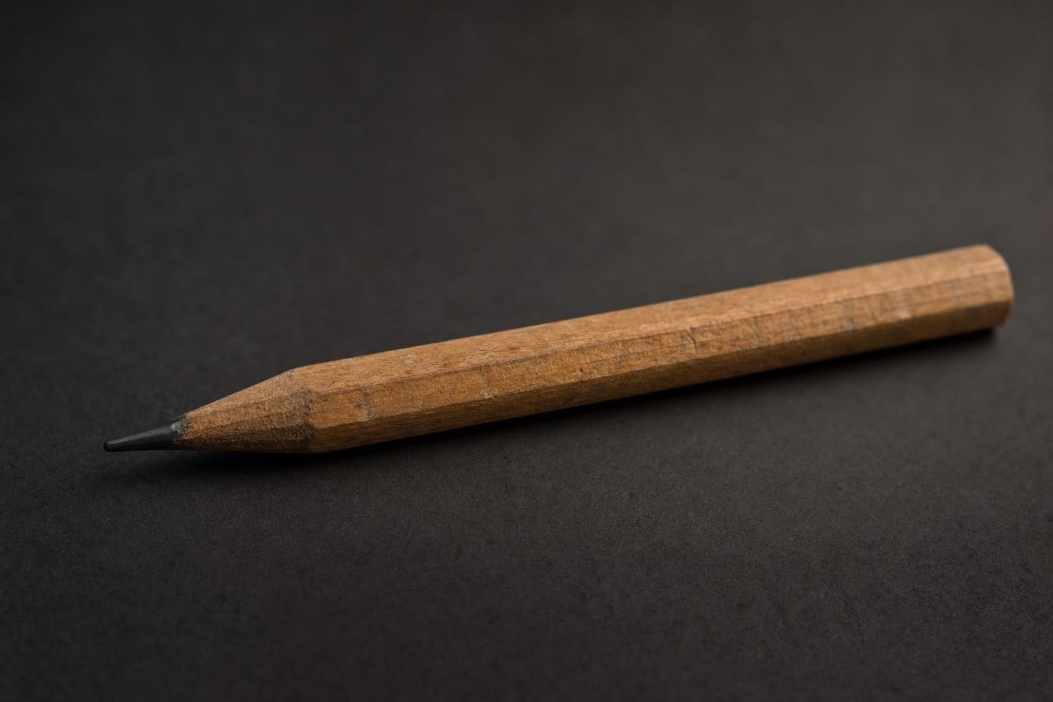 A single sharpened carpenter pencil resting under warm light against a dark background