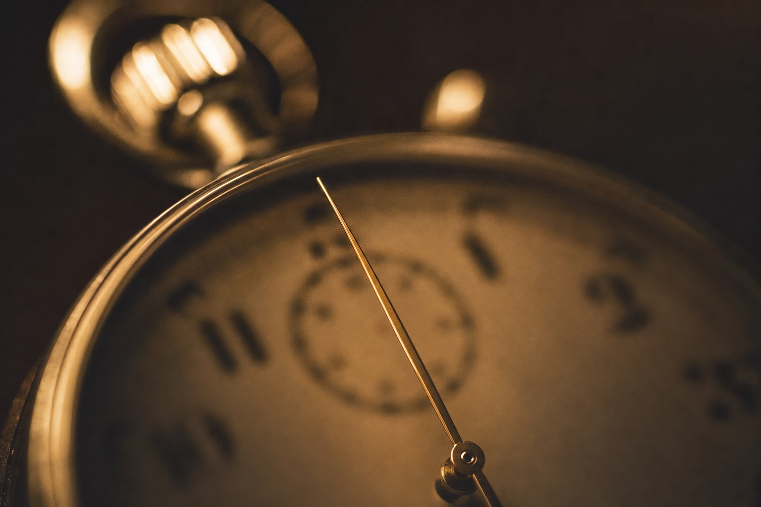 A vintage chrome stopwatch glowing warm against a dark background, its slender hand frozen near the top of the dial.