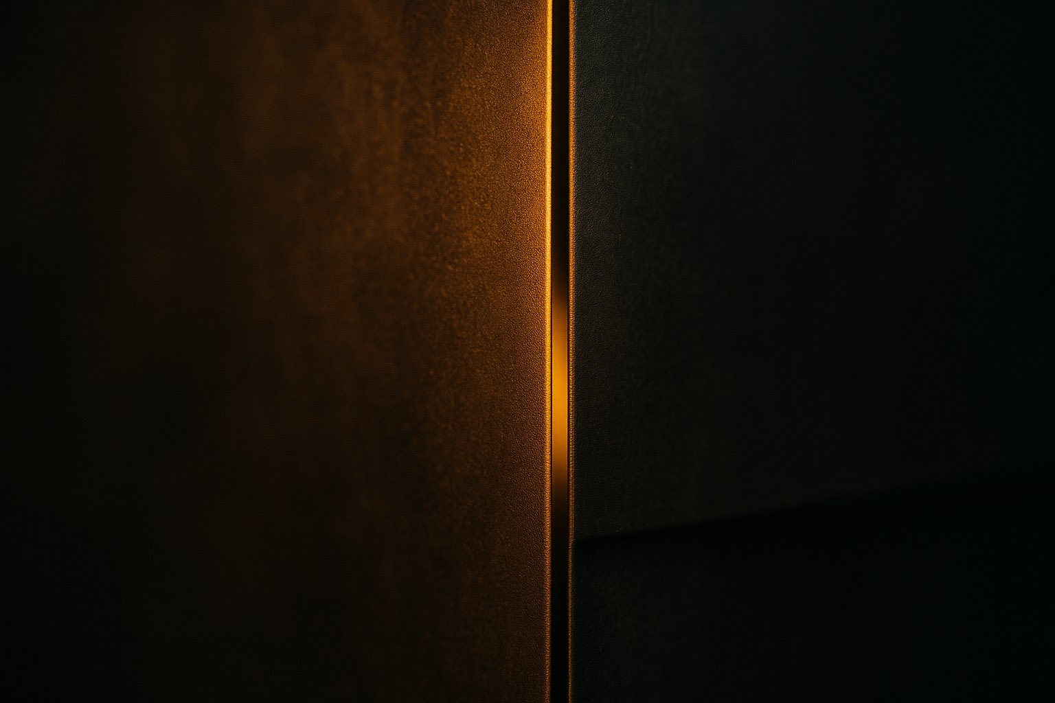 A steel wall dividing two dark spaces, a seam of warm light along the edge.